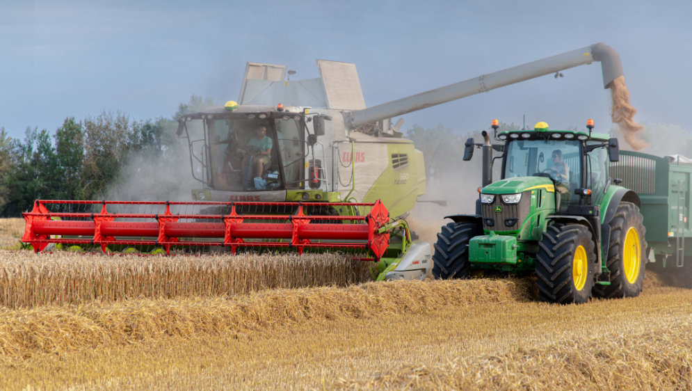 A combinr harvester, harvesting crops into the trailer of a tractor.